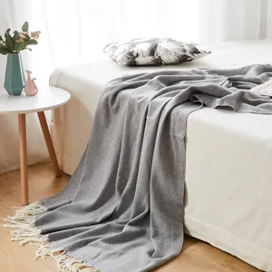 Grey herringbone throw blanket with fringe, soft woven knitted bed cover for home decor.
