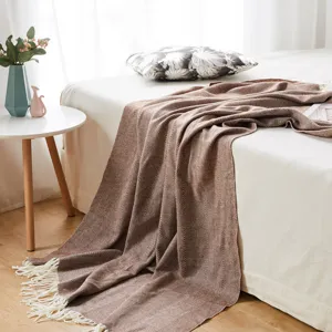 Detail shot of woven herringbone throw blanket with fringe on bed in cozy bedroom setting.