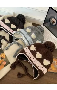 Close-up detail of cozy winter knitted earflap hats with cute heart patterns and fluffy pom-poms.