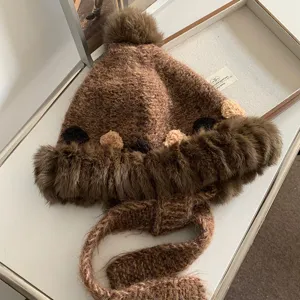 Brown knitted plush winter earflap hat detail showing soft wool texture and cute pom-pom design.