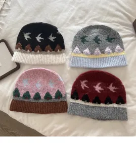 Nahaufnahme von vier bunten Retro-Jacquard-Strickmützen mit warmem Winter-Vogel-Baum-Muster.
