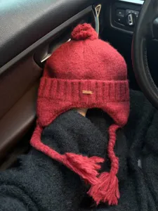 Cozy red knit earflap beanie with cute pompom and braided ties, warm winter fashion hat.