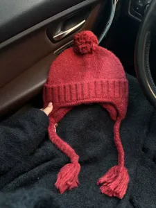 Close-up texture detail of the red knitted earflap hat with cute pom-pom and braided ties.