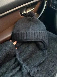 Black knitted earflap beanie with pom pom and braids, cozy winter windproof hat detail.