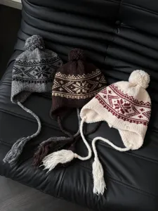 Detailed shot of winter warm knit earflap beanies with Nordic jacquard patterns and cute pompoms.