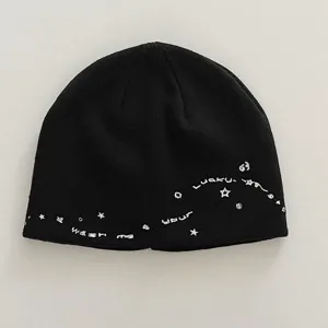 Black knit beanie hat detail with white star and letter embroidery, cozy winter style.