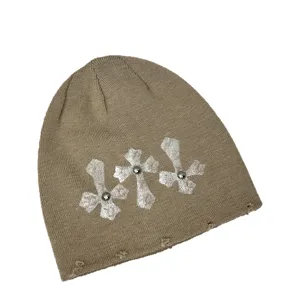 Detailansicht der khakifarbigen Strickmütze mit silbernen Kreuzen und Nieten im Streetwear-Stil.