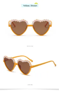 Children's heart-shaped sunglasses with floral lace trim, yellow frame and brown lenses detail.