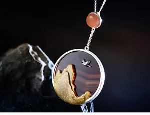 Gros plan détaillé du pendentif grue et montagne, mettant en valeur un savoir-faire argenté.