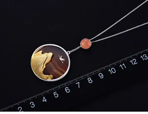 Gros plan détail du collier pendentif grue coucher de soleil argent avec agate et échelle.