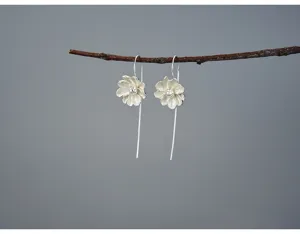 Detailed view of sterling silver flower drop earrings hanging on a rustic branch prop.