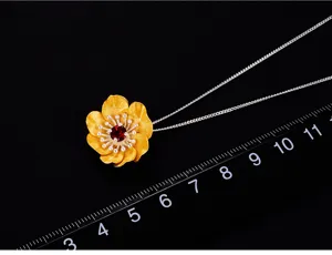 Primo piano di un ciondolo floreale in argento fatto a mano con gemma rossa centrale.