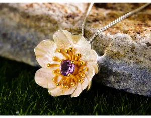 Dettaglio ciondolo fiore in argento con gemma viola e texture di stami dorati raffinata.