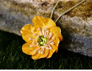 Primo piano dettagliato del raffinato ciondolo floreale dorato con gemma verde sulla roccia.