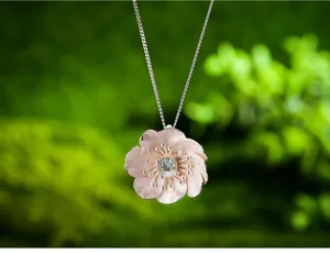 Primo piano dettagliato di una delicata collana con ciondolo a fiore in argento e gemma verde.