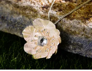 Collana con ciondolo a fiore in argento con dettaglio cristallo su sfondo in pietra.