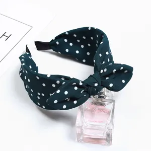 Close-up detail shot of dark green polka dot bow headband, cute rabbit ear style hair hoop.