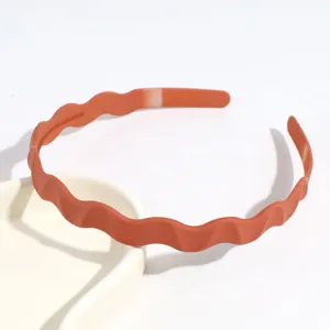 Gros plan sur le serre-tête ondulé minimaliste en plastique terracotta, accessoire idéal.
