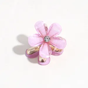 Close-up of a cute mini pink flower hair claw clip with rhinestone center and gold metallic base.