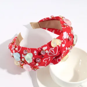 Red fabric heart knotted headband closeup, decorated with dazzling rhinestones and pearls.