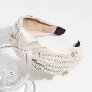 Detail shot of a chic beige satin knotted headband adorned with pearls and sparkly rhinestones.