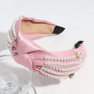 Close-up detail of a chic pink satin knotted headband adorned with elegant pearls and sparkling rhinestones.