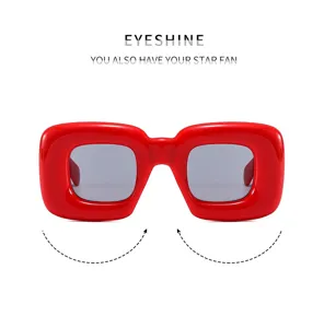 Close-up detail of bold red puffy square sunglasses showing smooth glossy frame and UV lenses.