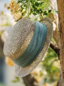 Detailed view of the vintage straw hat hanging on a tree branch with green ribbon.