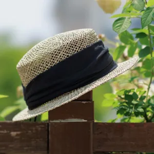 Detail view of the French retro woven flat top straw hat with black band for summer beach.
