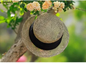 Detailed shot of a French retro hollow woven straw boater hat with black ribbon in garden.
