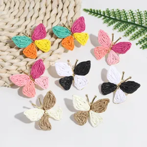 Colorful raffia straw woven butterfly earrings with gold frame, boho style nature detail shot.