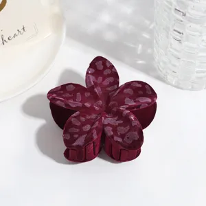 Gros plan détaillé d'une pince à cheveux fleur en velours rouge foncé à motif léopard.