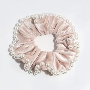 Primo piano dettaglio di un morbido scrunchie di velluto rosa con perle bianche eleganti.