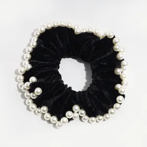 Dettaglio di un elastico per capelli in velluto nero con perle finte eleganti sul bordo.