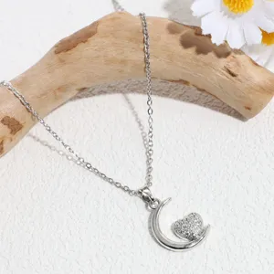 Close-up detail of silver crescent moon and crystal heart pendant necklace on wood.