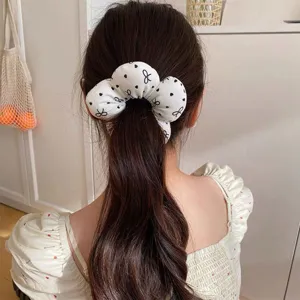 Close-up detail of a white cloud scrunchie with black bow print worn on dark ponytail.