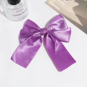 Closeup of a purple satin bow hair clip with elegant ribbon tail and secure clip detail.