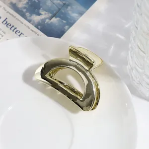 Close-up van een moderne geometrische gouden metalen haarklem op een wit bordje.