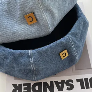 Denim beret close up detail, classic blue denim hat with stylish square metal logo accent.
