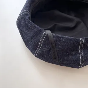 Detailed close-up view of the dark blue denim beret showcasing contrast stitching and fabric.