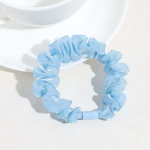 Gros plan sur un chouchou de cheveux bleu clair brillant avec un design plissé élégant.