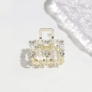 Detailed view of a small gold-tone metal hair claw clip adorned with pearls and rhinestones.