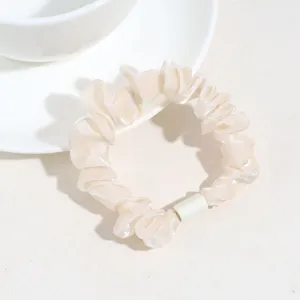 Gros plan détail d'un chouchou à cheveux en satin beige avec design plissé et anneau blanc.