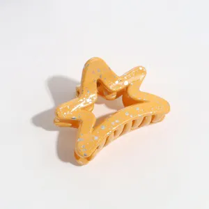 Close-up detail of a yellow star-shaped hair claw clip featuring stylish silver splatter design.