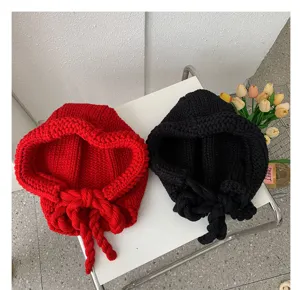 Detail shot of cozy knitted hooded hats with tie strings in red and black, winter warm earflap caps.