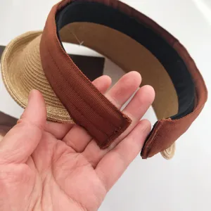 Vista de detalle cercana del sombrero de sol de paja con ribete de cinta marrón y banda interior.