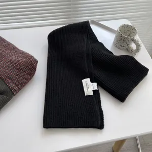 Primo piano del dettaglio della sciarpa in maglia nera con texture a coste ed etichetta.