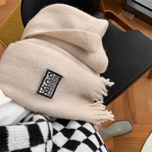 Beige knitted scarf detail featuring soft fabric, fringe trim and woven label for winter warmth.