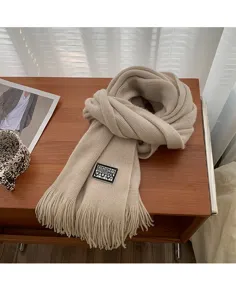 Beige knitted scarf detail featuring cozy texture, fringe ends and decorative label.