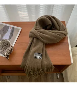Detailed shot of a cozy brown knitted winter scarf with fringe and stylish label on table.